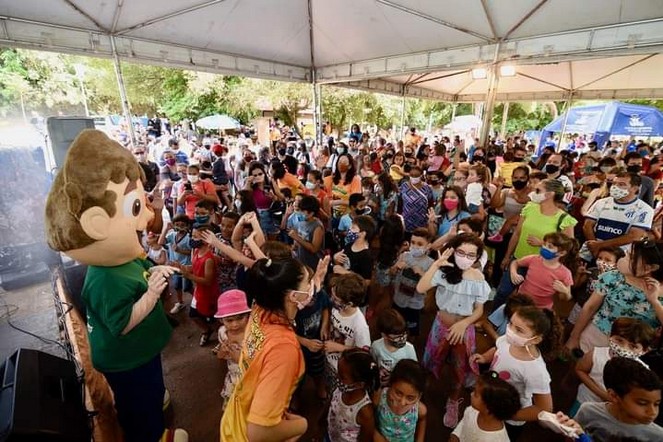 Mascote Recicladinho animando uma multidão de crianças e famílias em evento ao ar livre