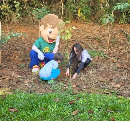 Mascote Recicladinho acompanhando o plantio de uma muda de árvore com uma família
