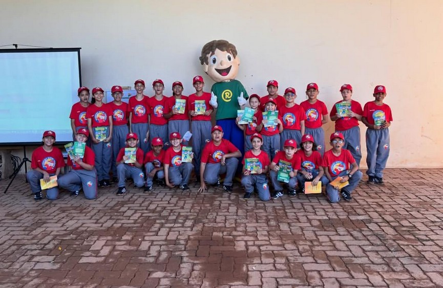 Turma de estudantes uniformizados segurando livros do Recicladinho ao lado do mascote